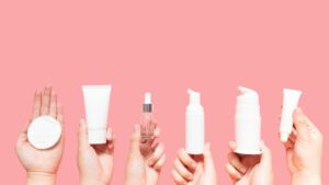 CBD skincare options, hands holding up creams, tinctures, and oils on pink background
