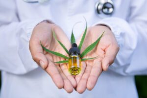 Doctor's hands holding a CBD oil bottle and hemp leaf