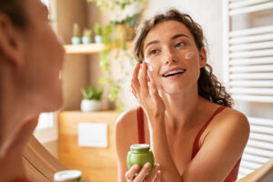Young woman applying clean beauty cream in mirror